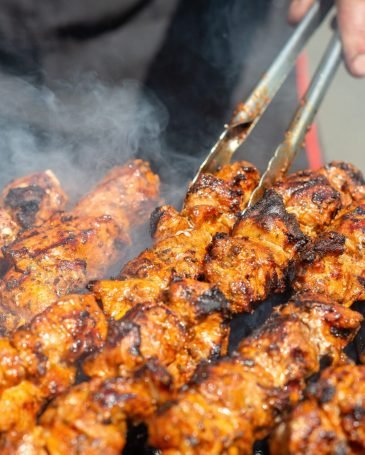 Meat on skewers fried on the grill in the open air, visible hands of the cook.
